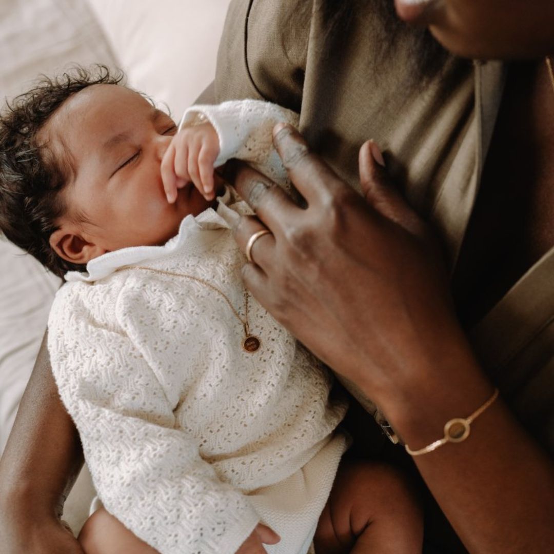 Petit bébé portant un collier médaille Madeleine, dormant dans les bras de sa maman 