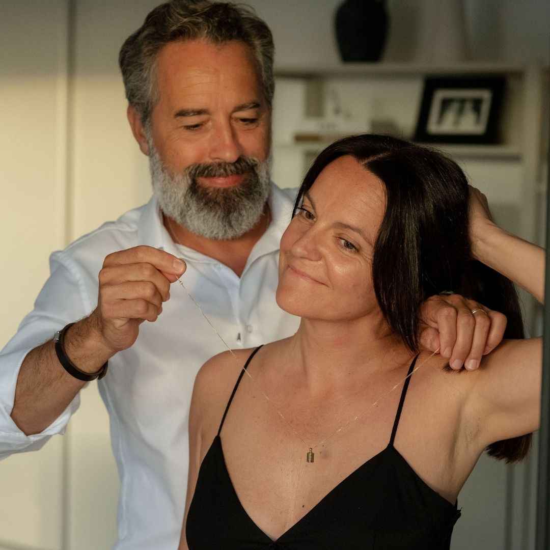 Un homme accrochant le collier Mon Petit Poids plaqué or jaune autour du cou de sa femme