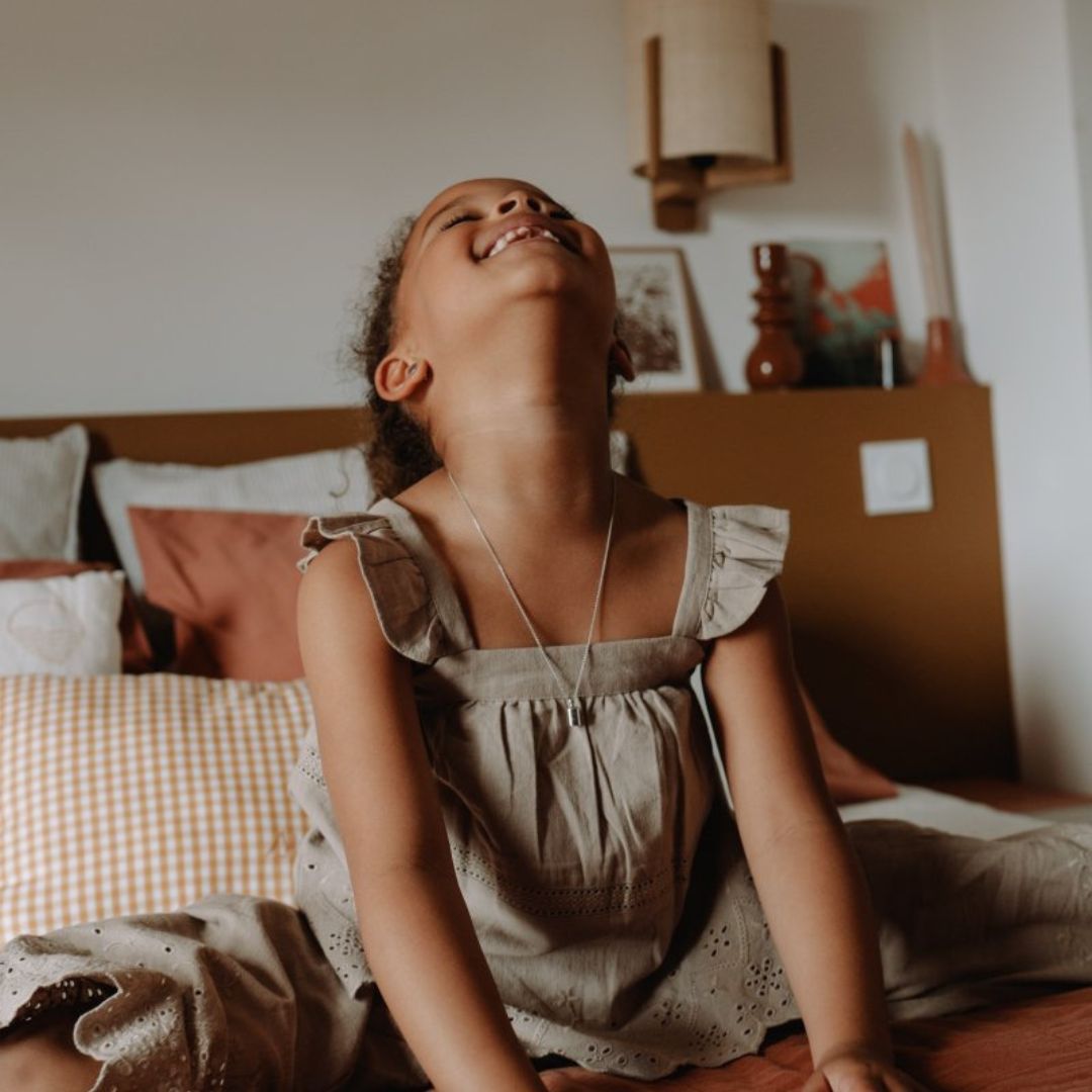 Collier Mon Petit Poids argenté rhodié porté par une petite fille souriant vêtue d'une robe grise