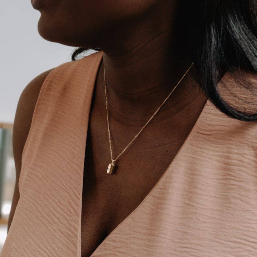 Collier Mon Petit Poids en plaqué or jauneporté autour du cou d'une femme portant un haut rose poudré