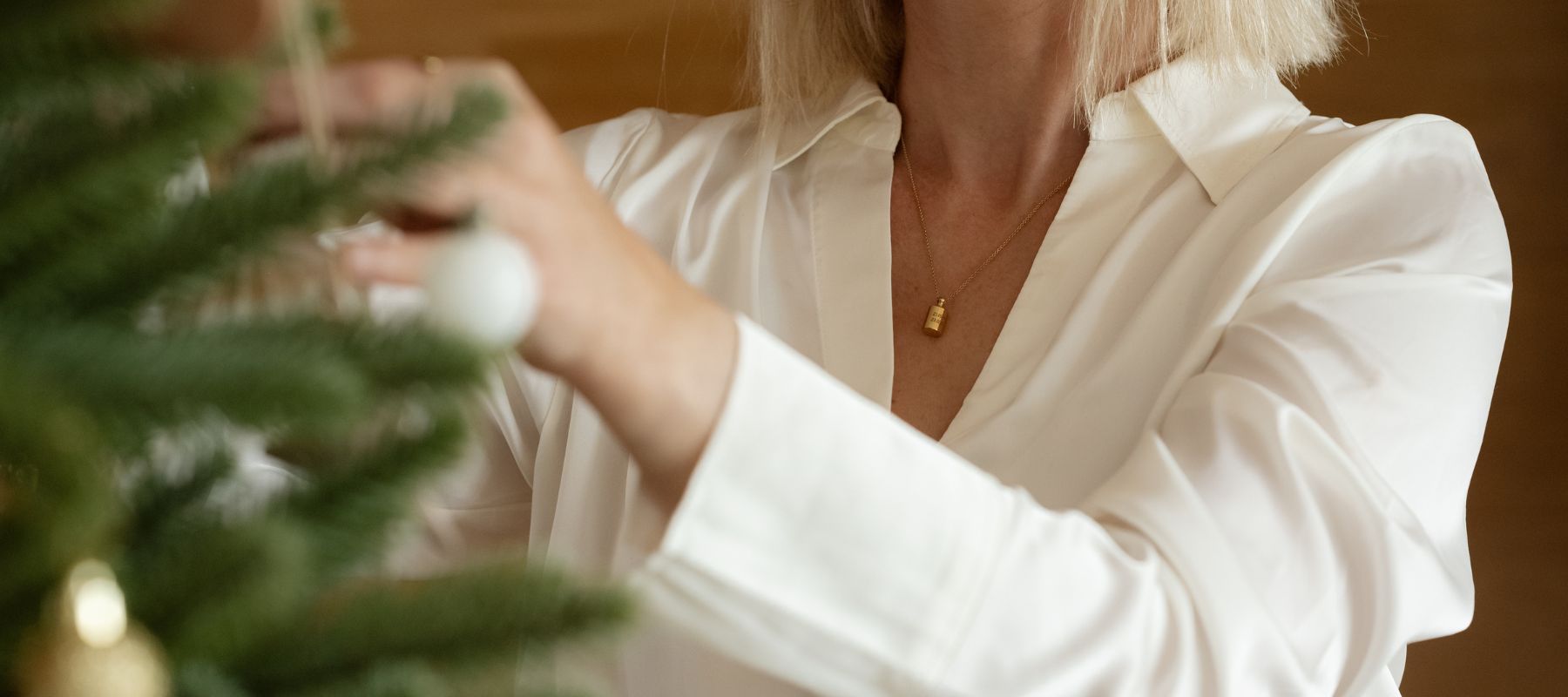 Collier Mon Petit Poids plaqué or jaune, porté par une femme décorant un sapin de Noël