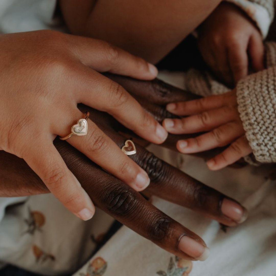 Bague Simone perlé sur le doigt d'un enfant dont la main est posée sur celle de sa mère. On voit une main de bébé à droite