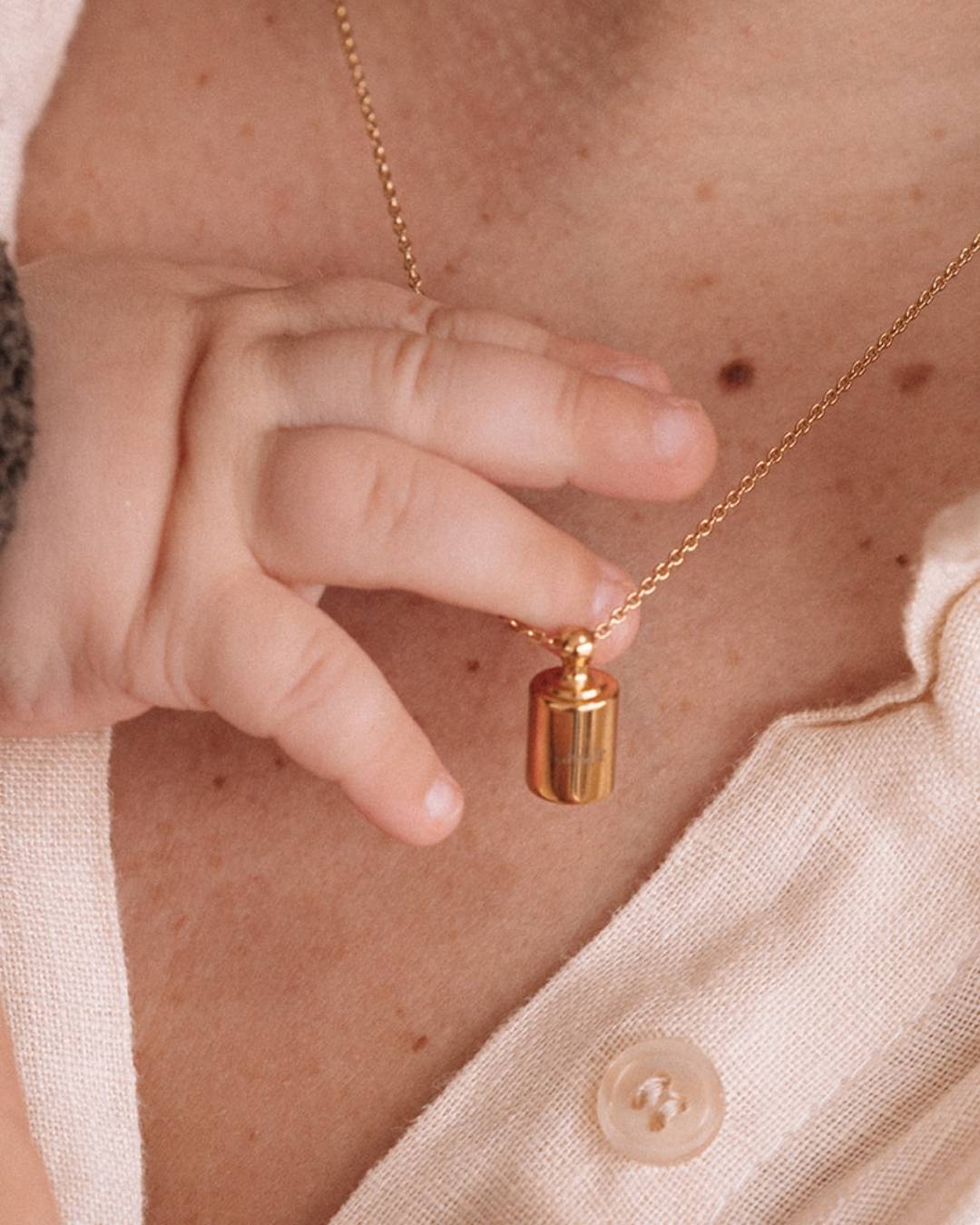 Main de bébé touchant un collier Mon Petit Poids porté par sa maman