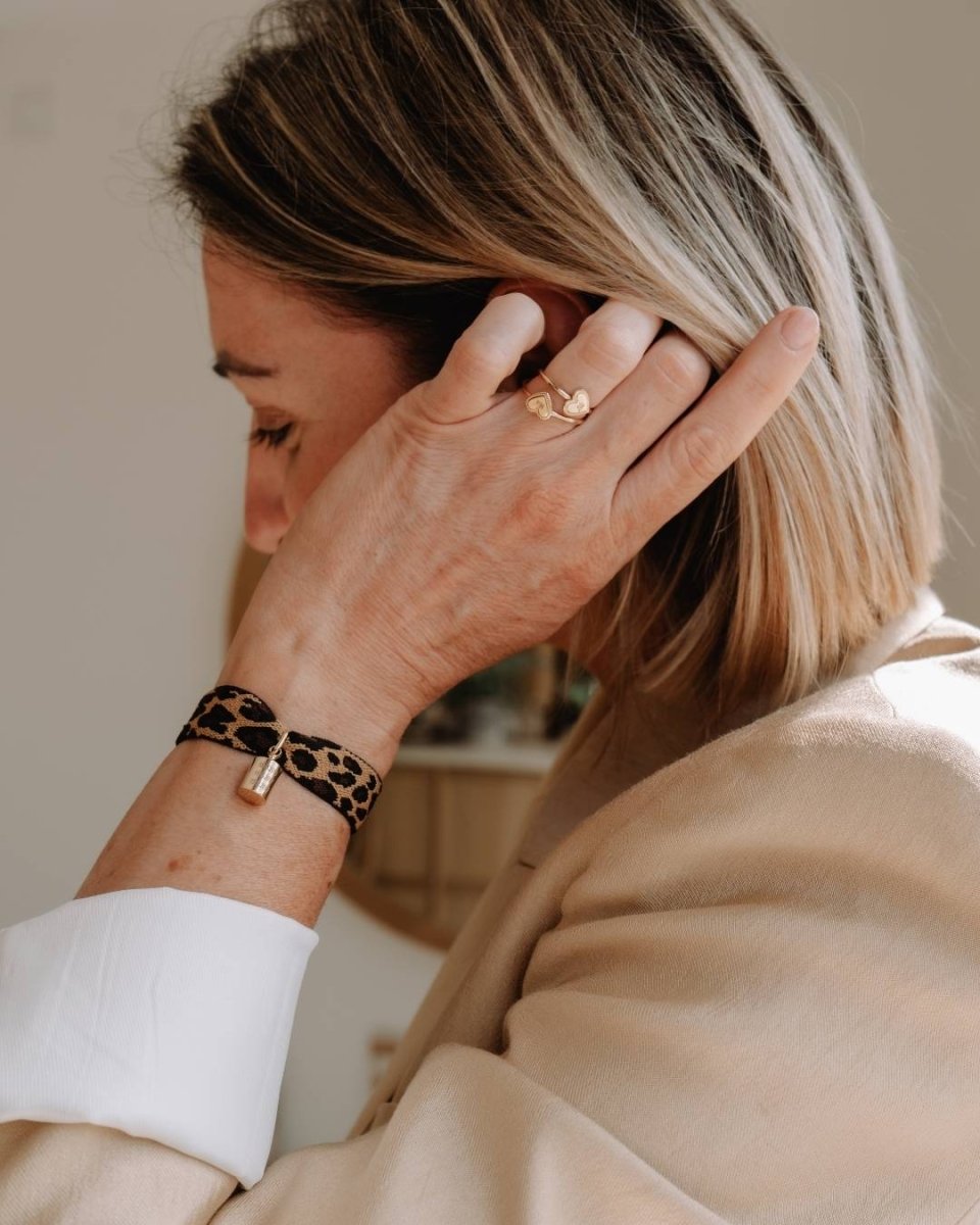 Femme ajustant ses cheveux en portant un bracelet Mon Petit Poids léopard personnalisé en plaqué or jaune avec pendentif gravé