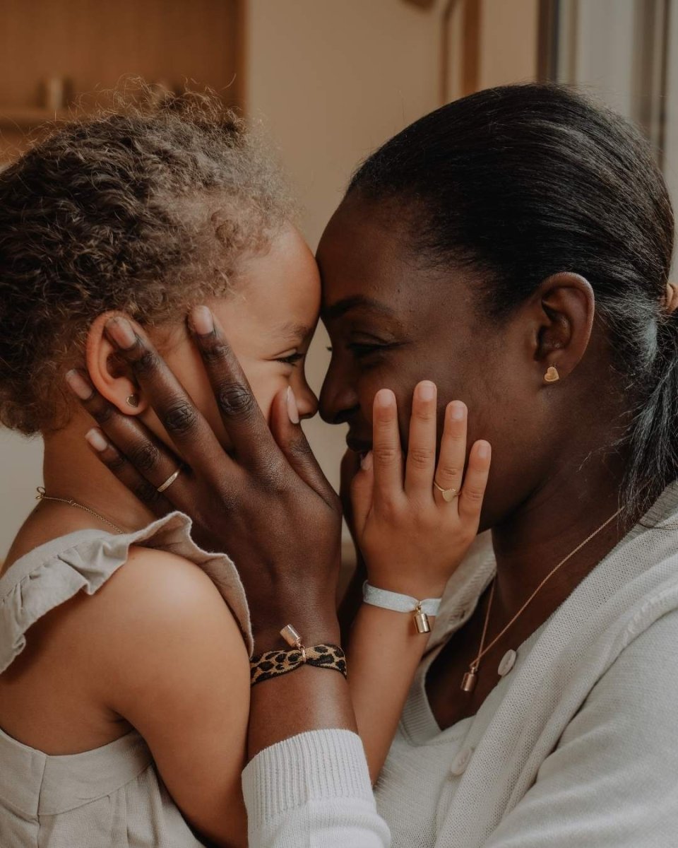 Maman portant le coffret bracelets Mon Petit Poids léopard en plaqué or jaune avec pendentif gravé personnalisé et bracelet ruban léopard, échangeant un moment tendre avec sa fille