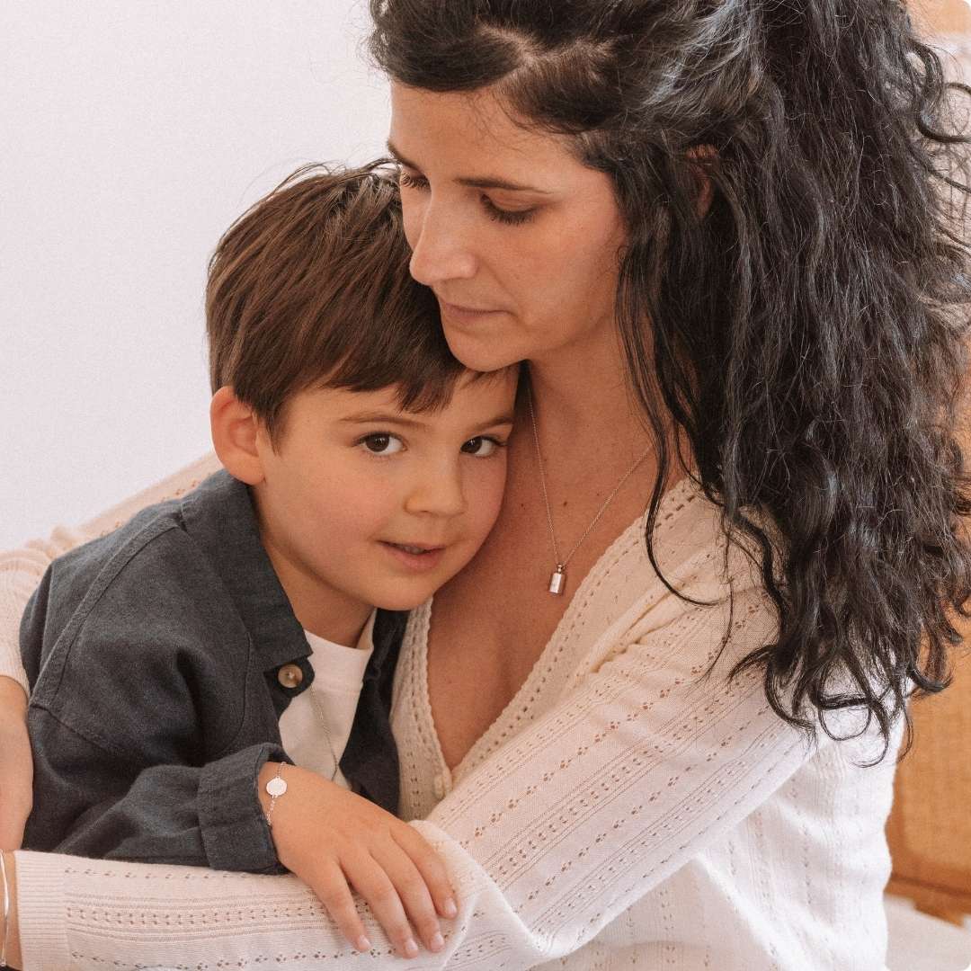 Une maman portant le collier Mon Petit Poids argenté rhodié fais à calin à son fils.