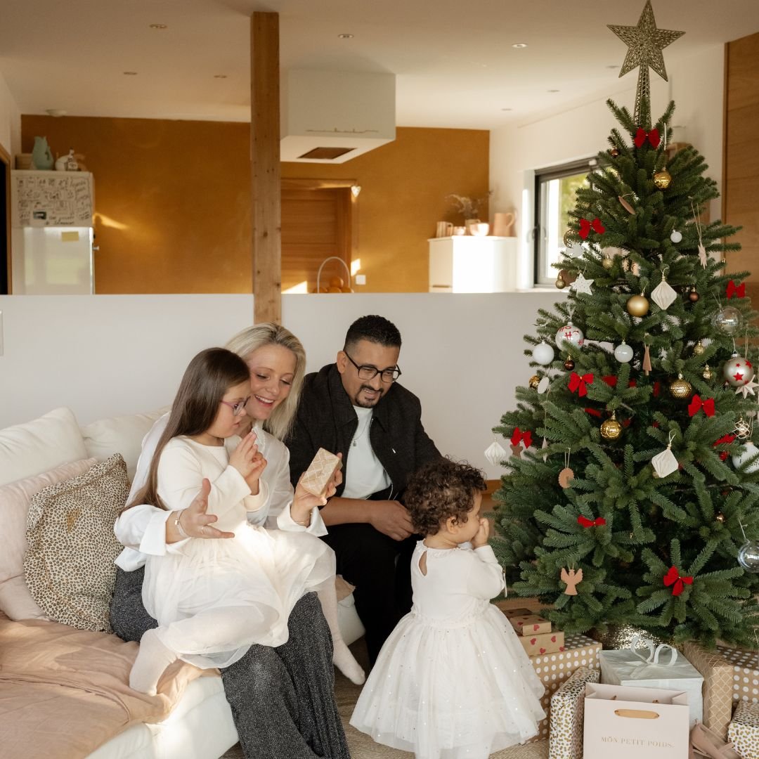 Famille avec deux enfants, assise sur un canapé, devant le sapin de Noël