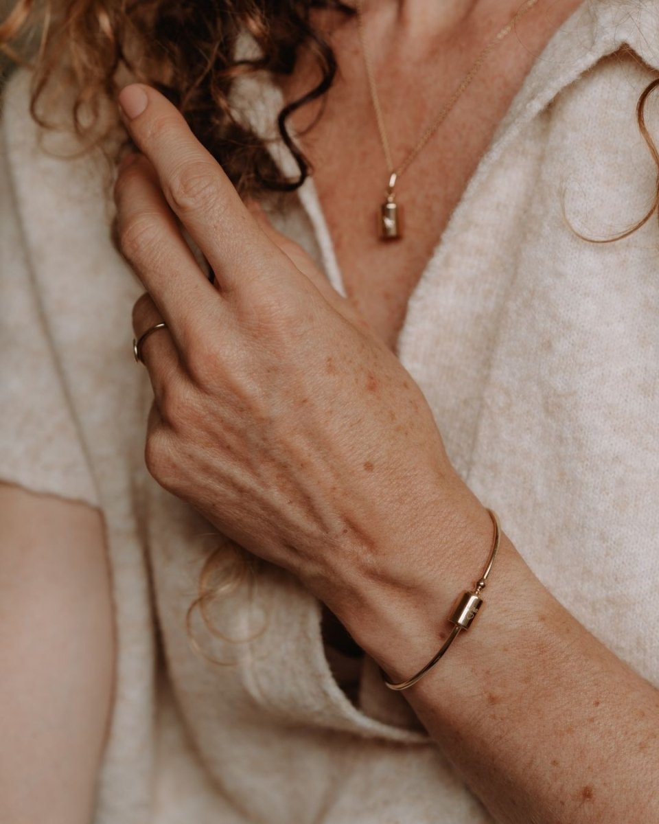 Femme touchant délicatement ses cheveux en portant le jonc Mon Petit Poids en plaqué or rose avec pendentif gravé personnalisé assorti à un collier Mon Petit Poids