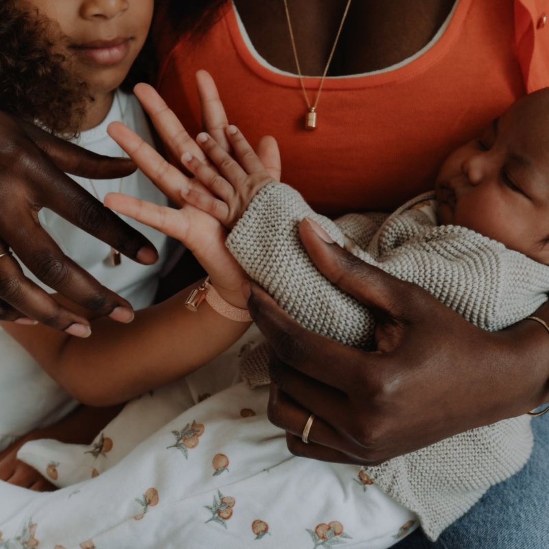 Une maman enlaçant ses eux enfants. La main de la petite fille appuyée contre celle du bébé